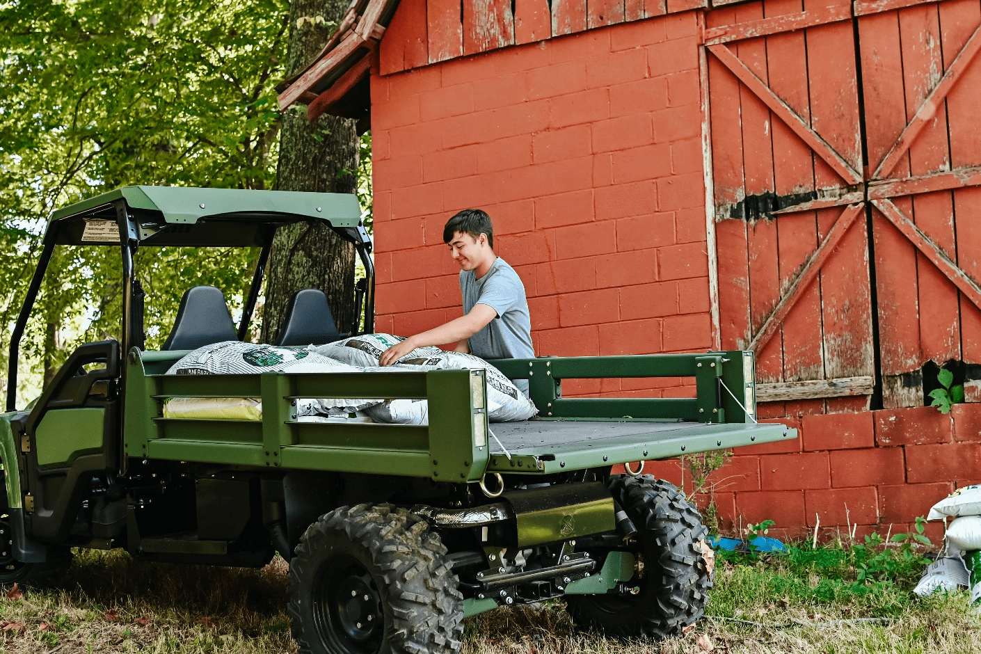 A person loads lawn care materials into the bed of a John Deere Gator Utility Vehicle