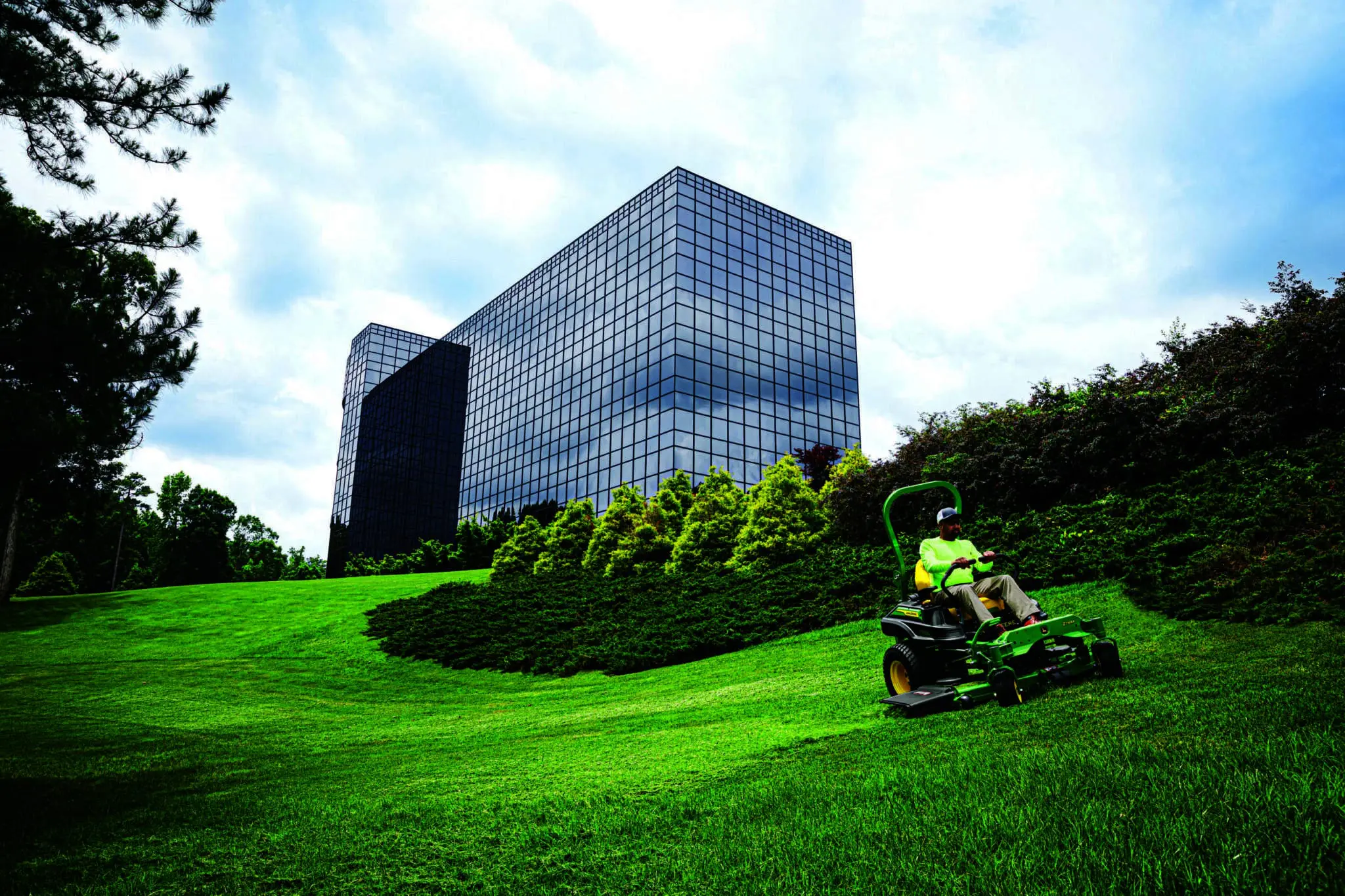 A landscape company mows along a hillside outside of an office building on a John Deere Z900 zero turn mower