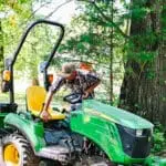 A person gets on a John Deere 1023E tractor with a spreader attachment