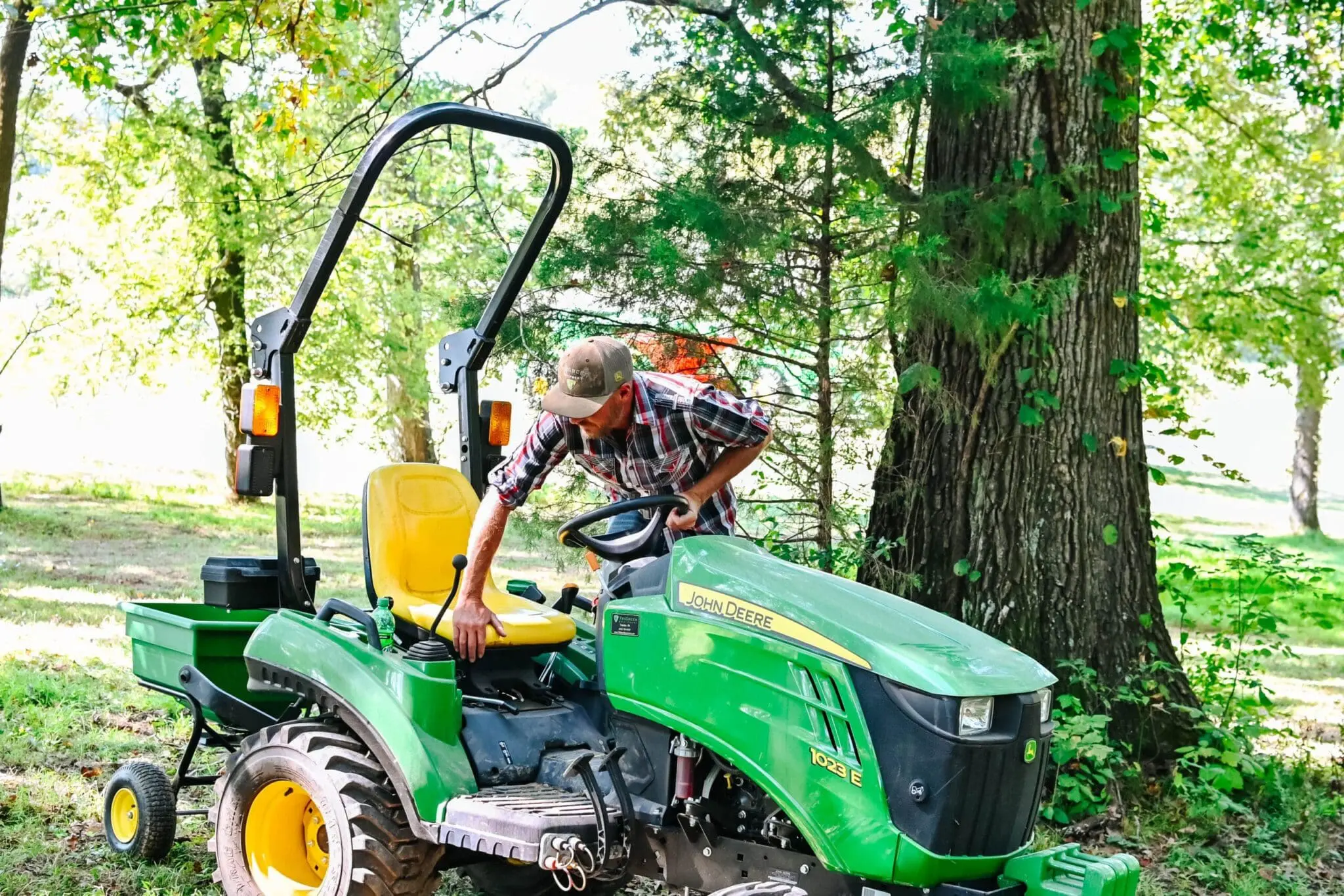 A person gets on a John Deere 1023E tractor with a spreader attachment