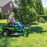 A woman mows a yard with a Z320M Deere zero turn