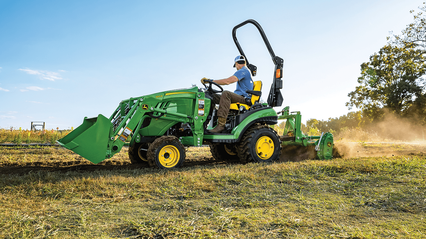 A person tills the ground with a John Deere 1025R tractor