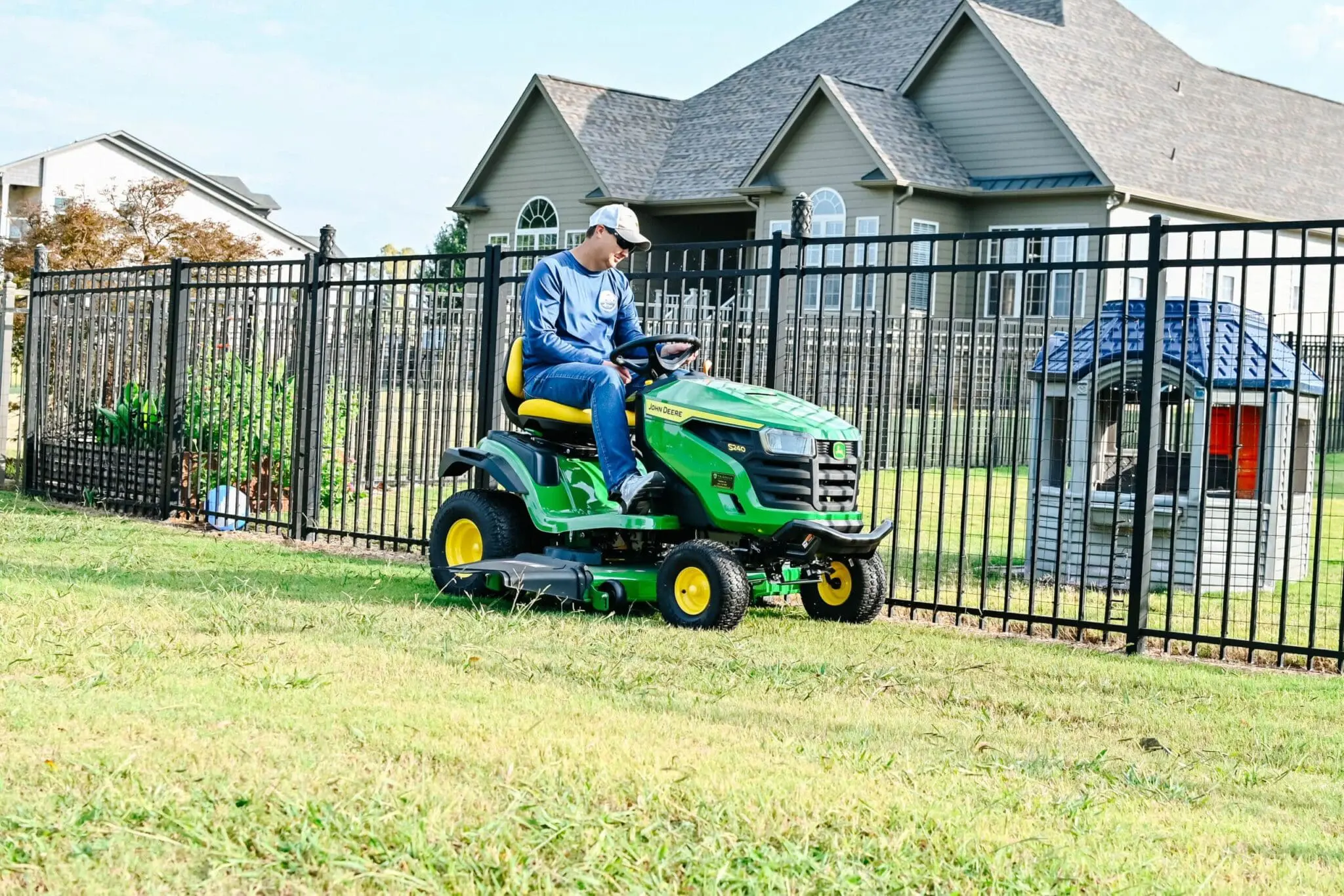 A man drives a John Deere S140 riding lawn mower in a backyard in Alabama