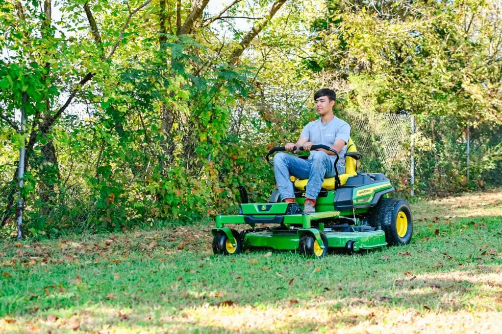A man drives a John Deere zero turn mower