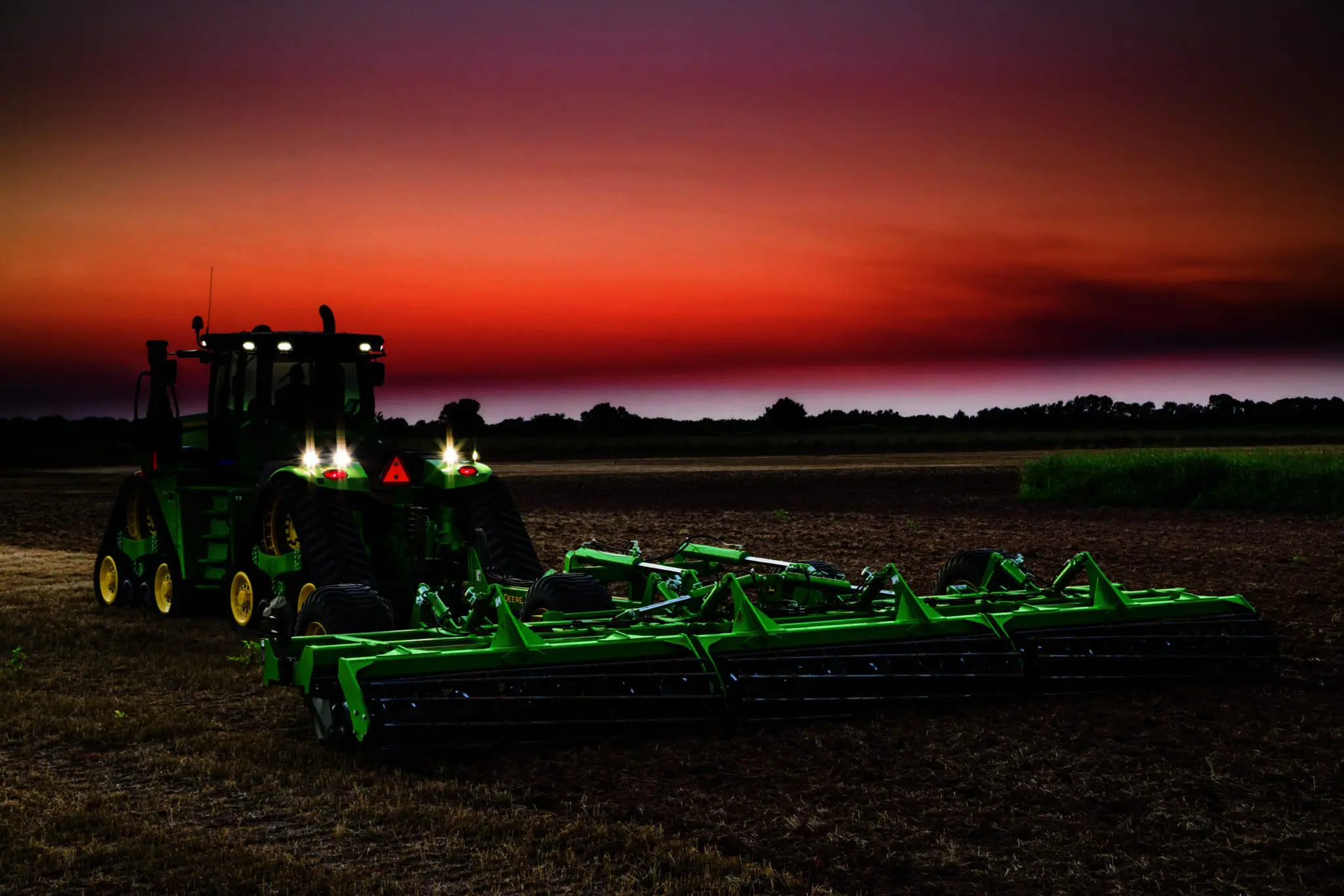 A John Deere 2680H disk pulled by a tractor does tillage work in a farm field at sunset