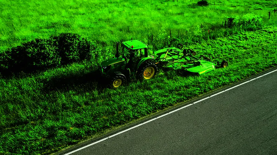 John Deere 6M tractor mows grass on a roadside