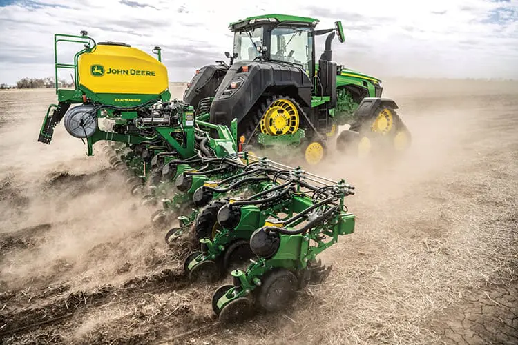 A John Deere 8RX tractor with liquid tanks pulls a planter in a farm field