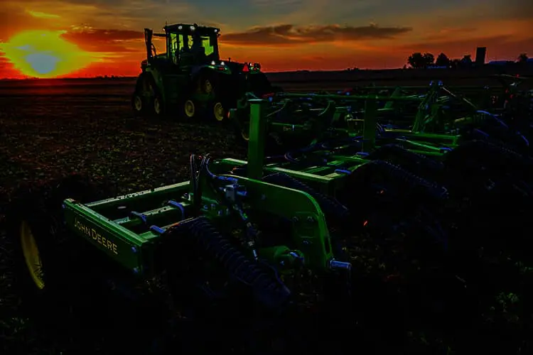 A John Deere tractor and nutrient applicator toolbar in a farm field at sunset.