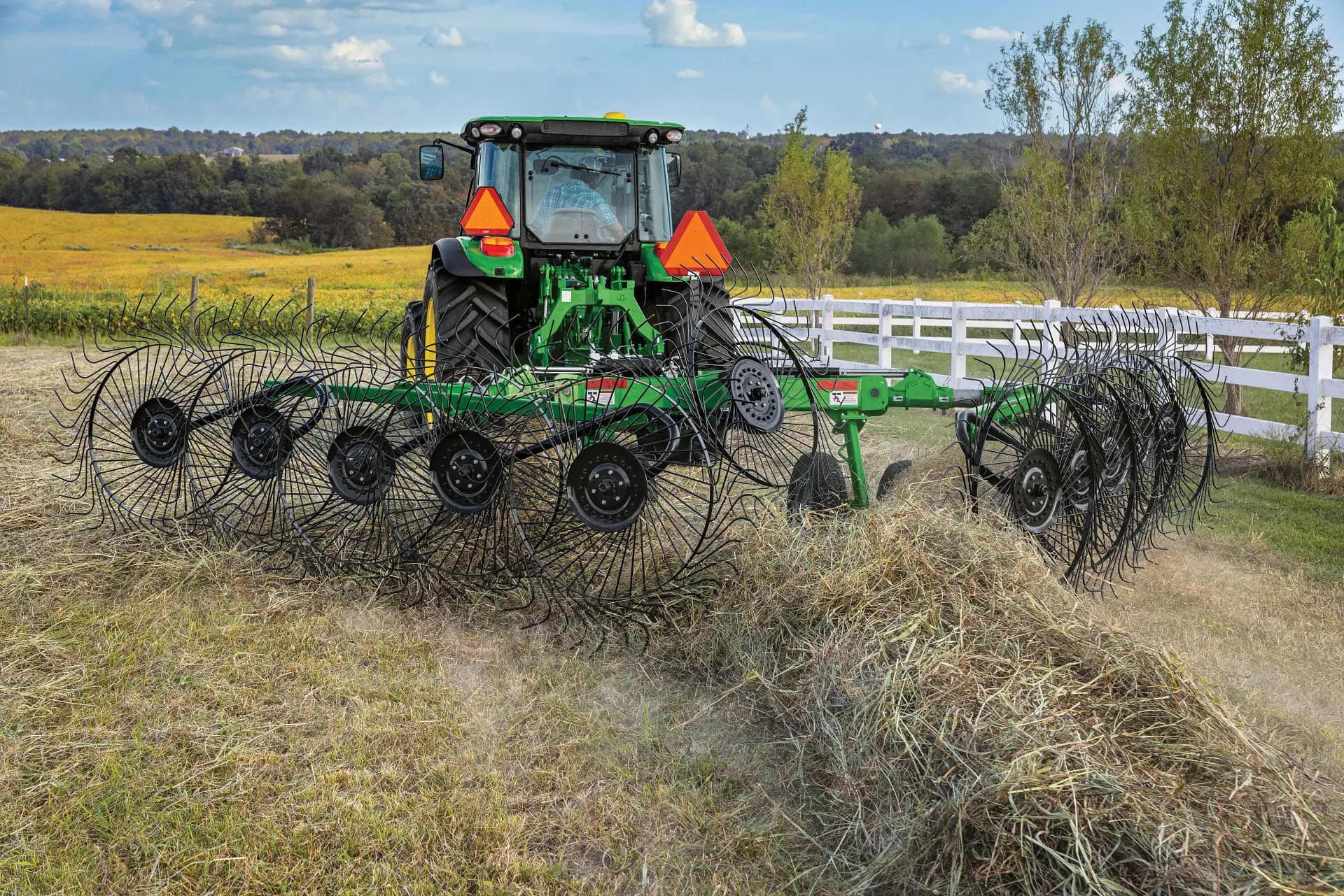 John Deere tractor windrows hay with Frontier wheel rake
