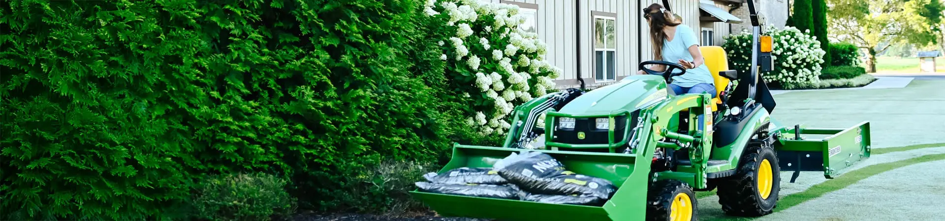A person moves mulch with a John Deere 1025R 1 series compact utility tractor