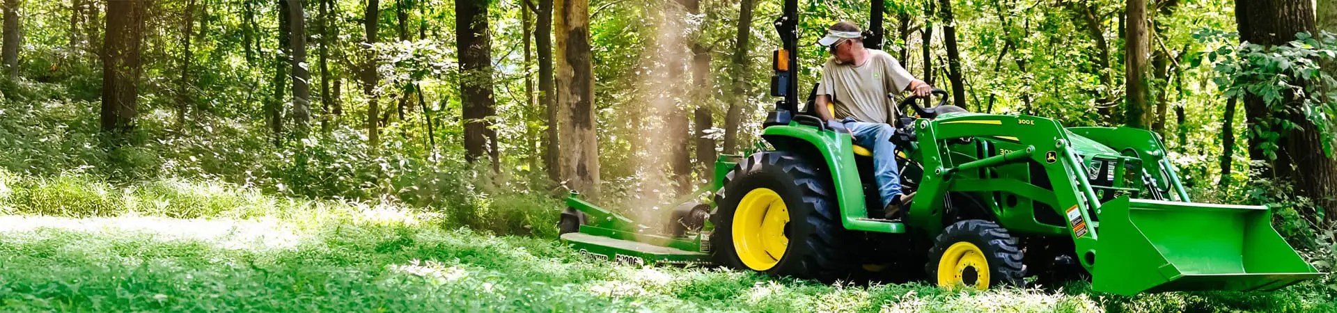 Technician operating 3 series compact tractor in wooded area.