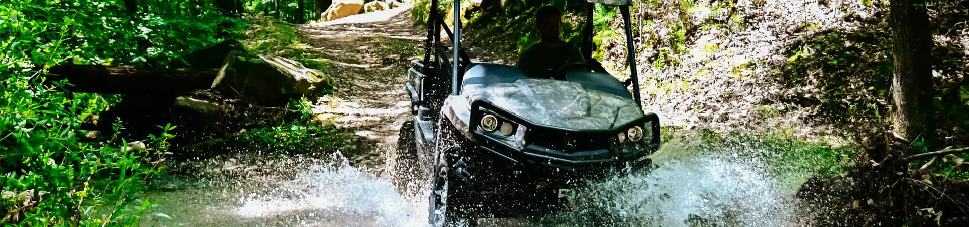 A John Deere 560M side by side drives through a creek off-road