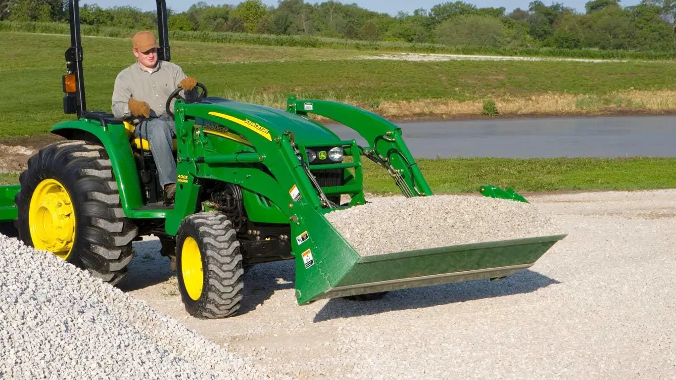 Man drives John Deere compact tractor with 4-in-1 bucket