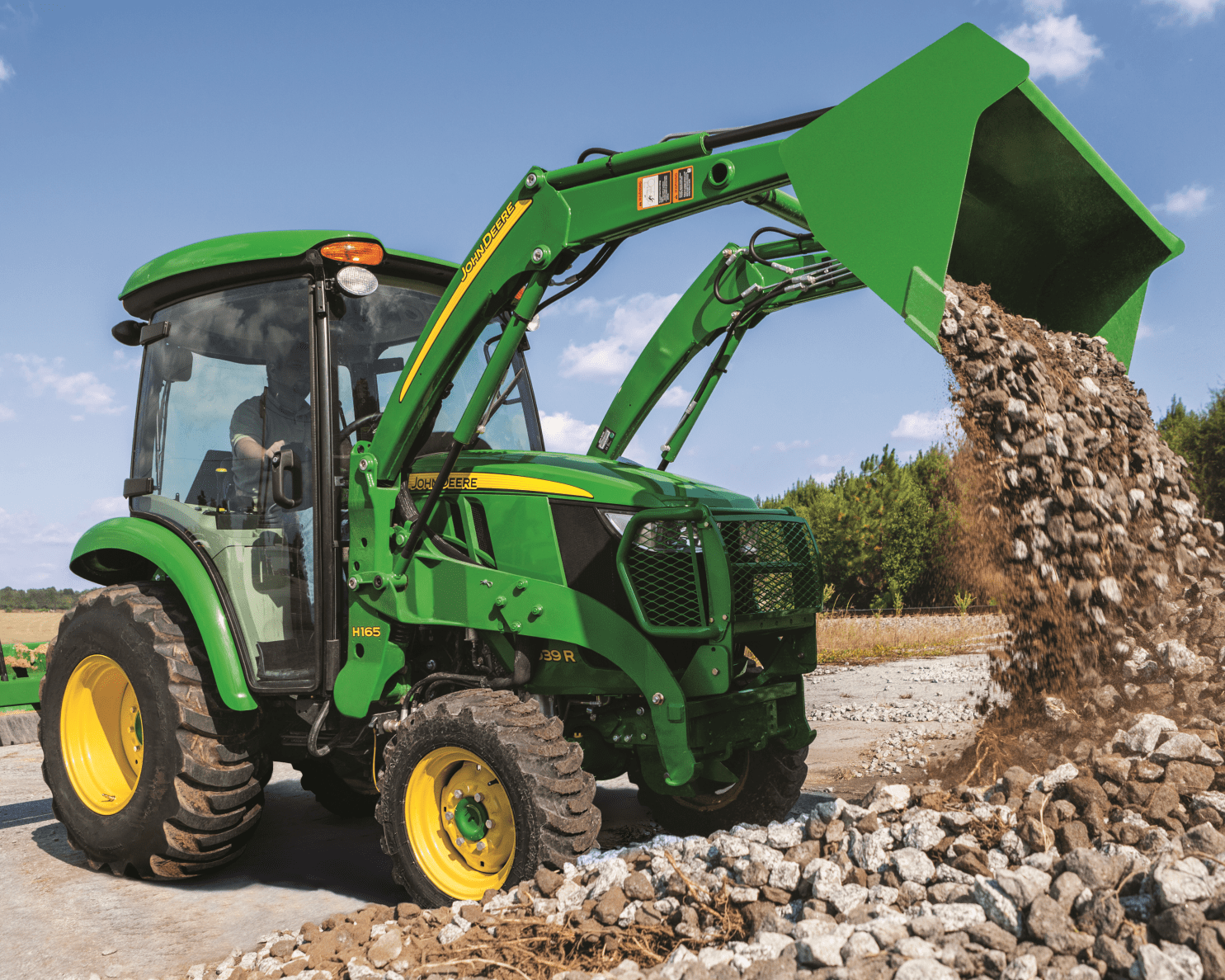 A person dumps a load of gravel with a 3R tractor