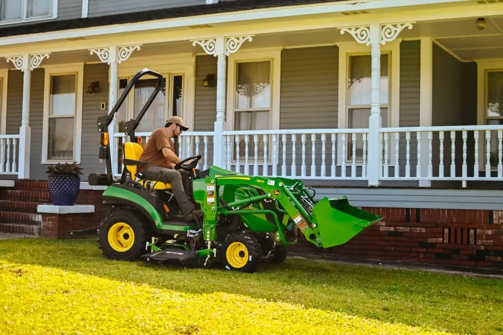 A man mows with a Deere 1025R loader mower tractor next to a house in Alabama