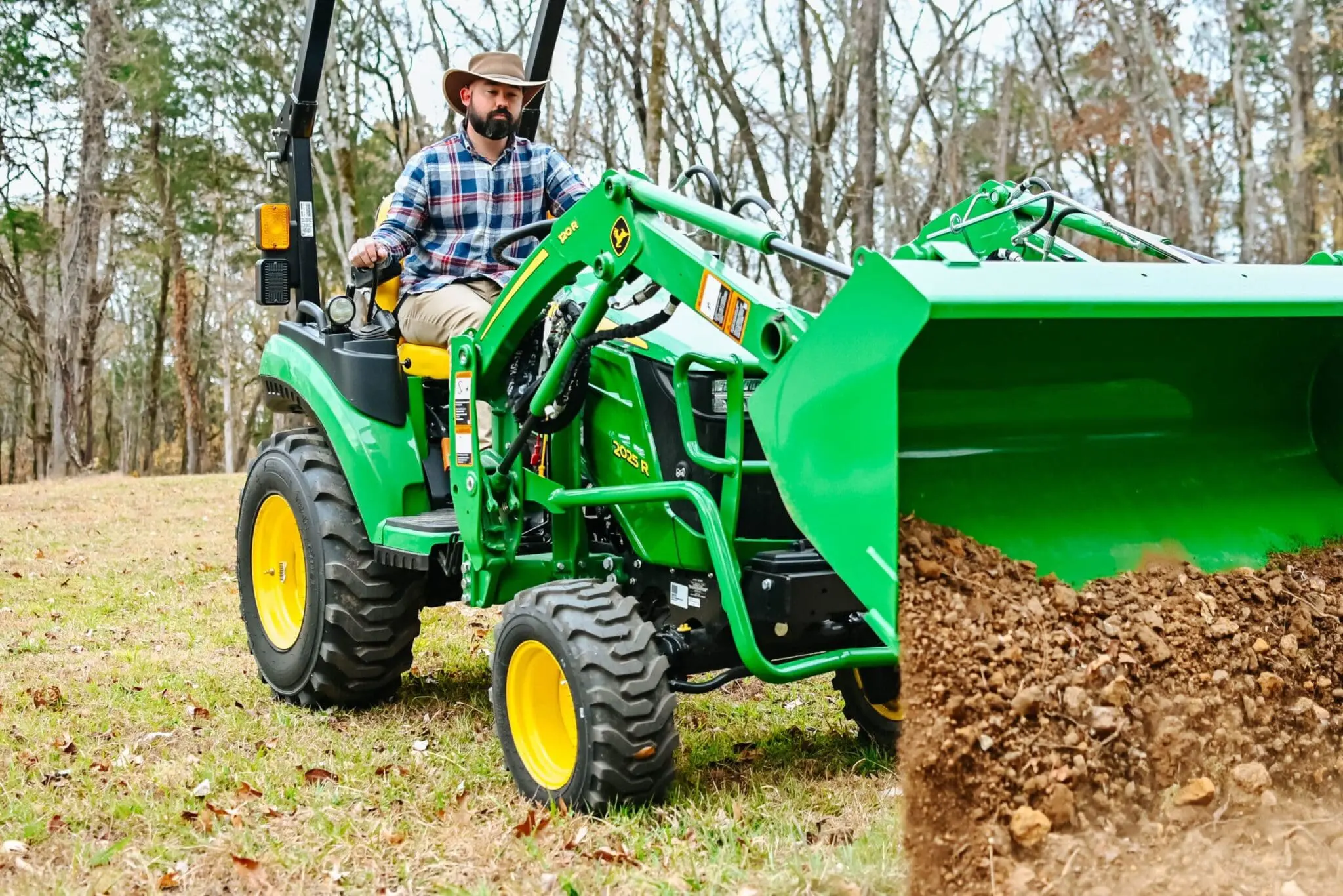 A person moves dirt with a John Deere 2R tractor and loader