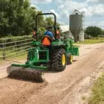 A person repairs a road with a John Deere small tractor