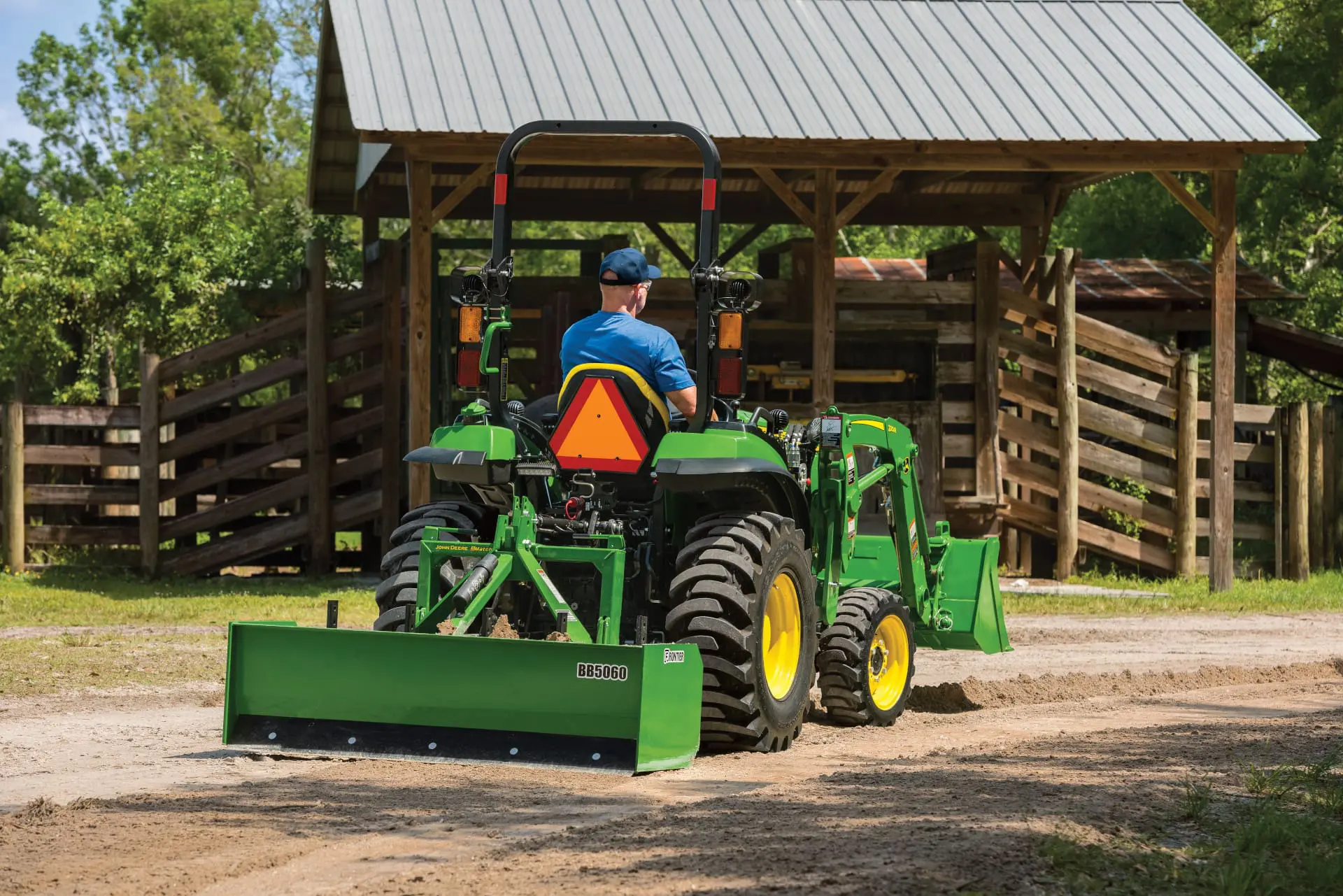 A person grades a gravel area with a John Deere small tractor and box blade