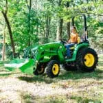 A woman moves mulch bags with a John Deere 3038E tractor