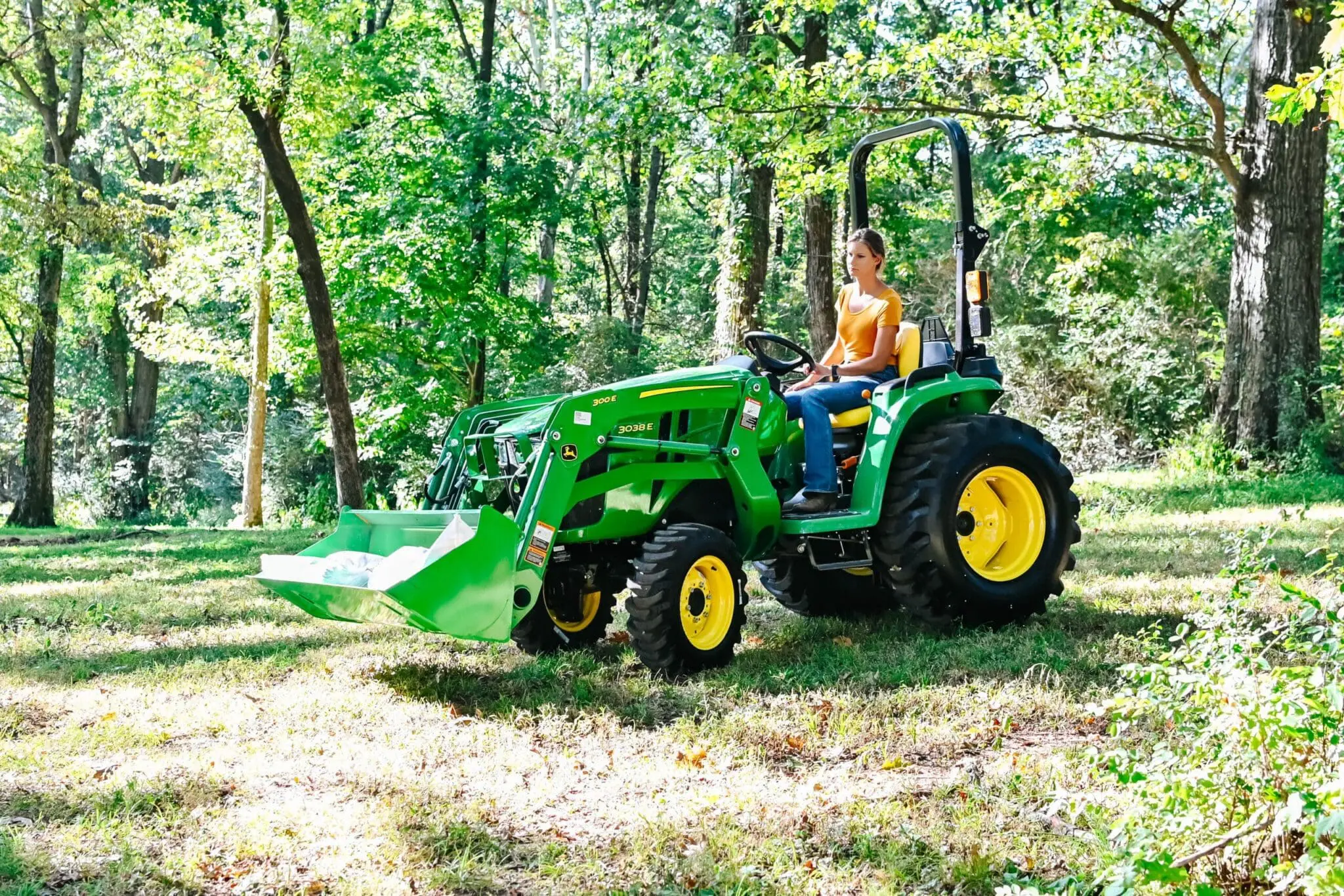 A woman moves mulch bags with a John Deere 3038E tractor
