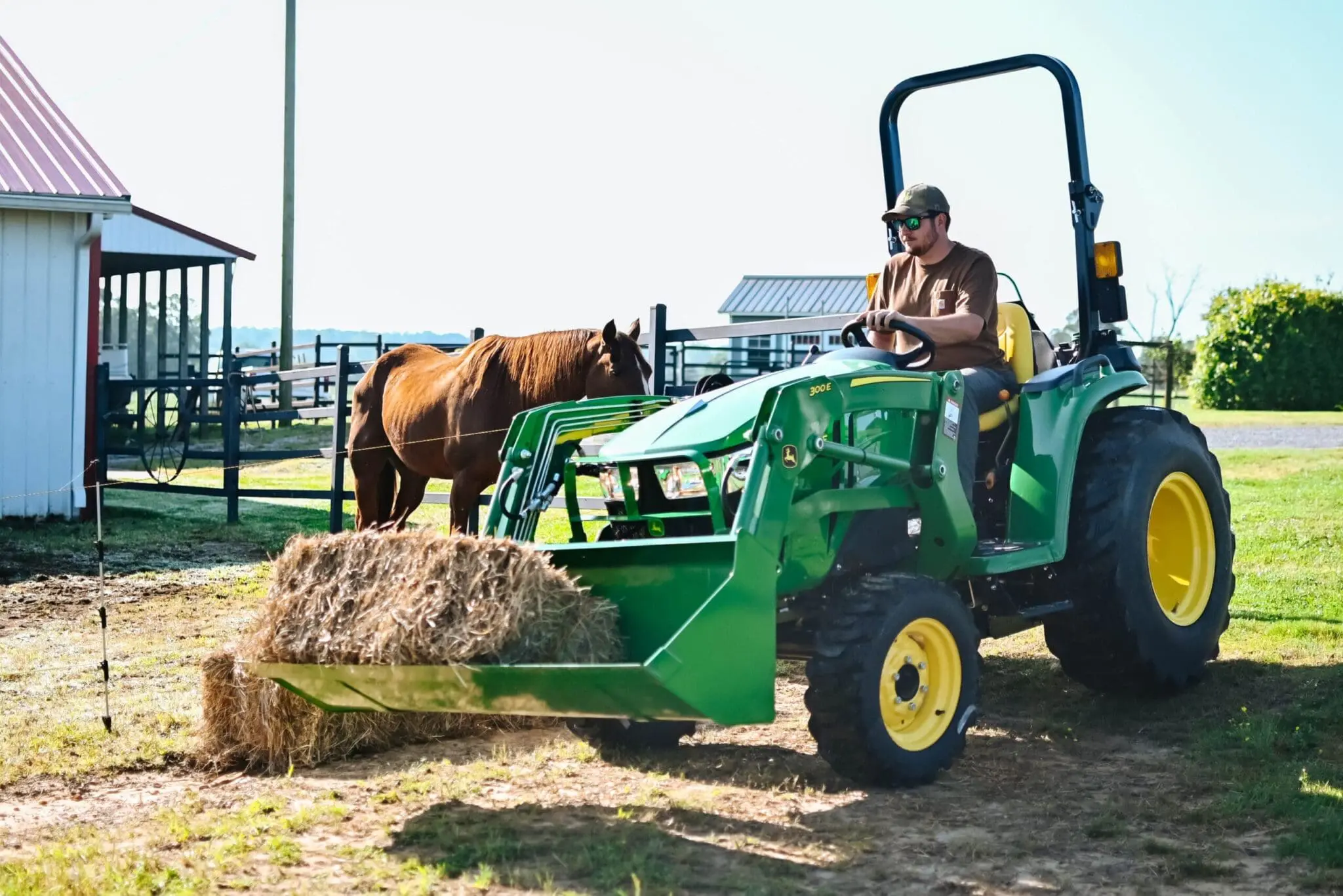 A man moves hay into a horse pasture with a John Deere 3E tractor