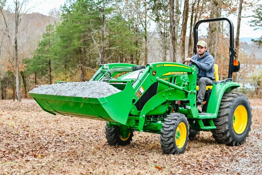 A man moves a load of gravel with a John Deere 3046R tractor and loader