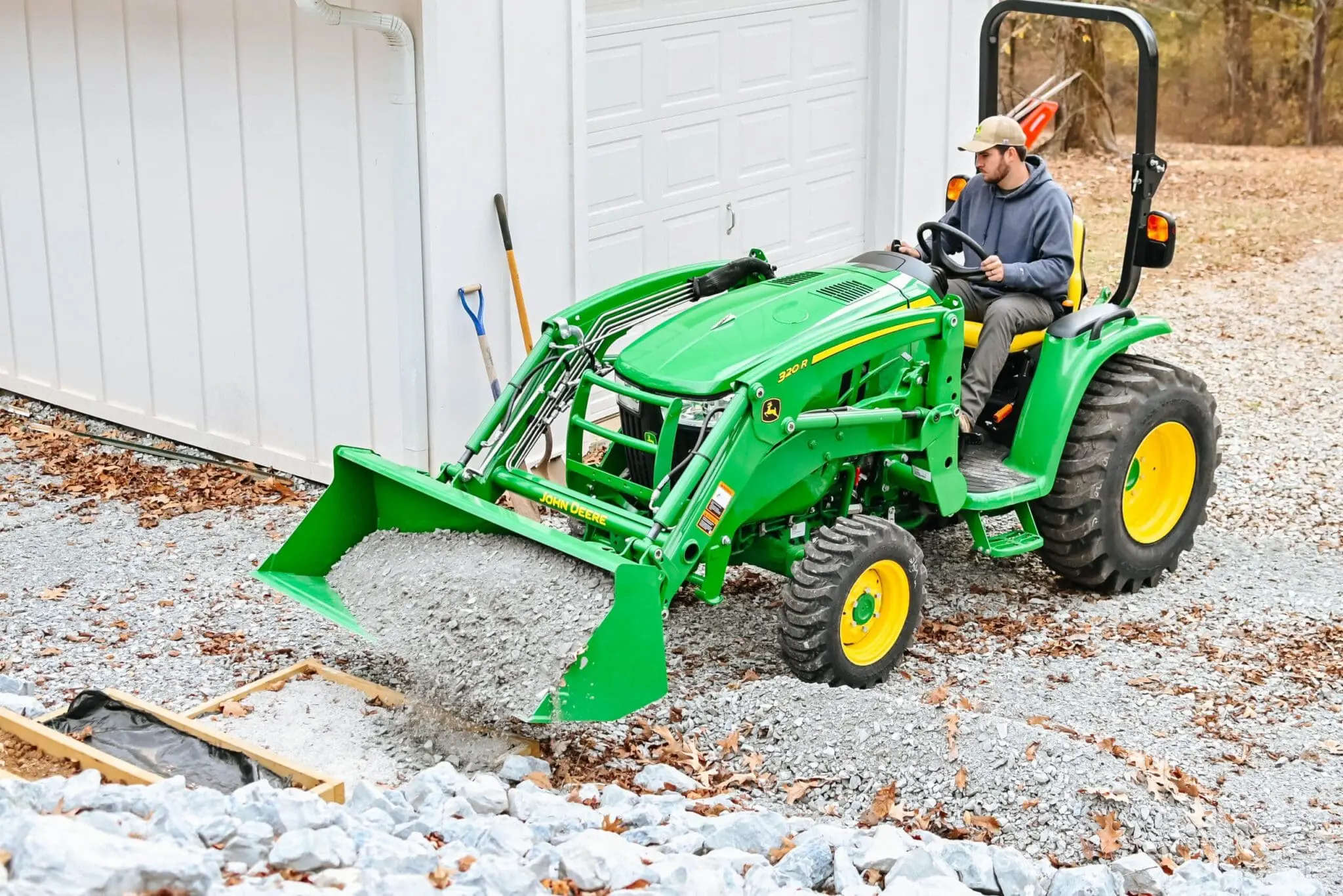 A man moves gravel with a John Deere 3R tractor loader