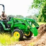 A man on a John Deere 4M tractor loader lifts a load of dirt