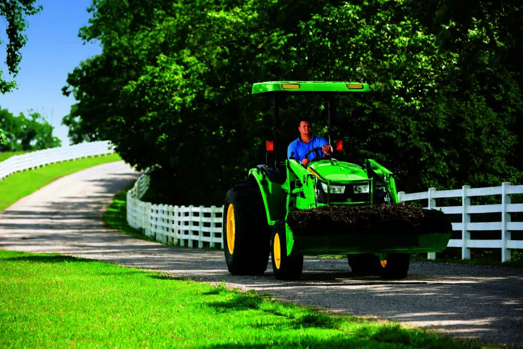 A John Deere tractor loader carrying dirt on a driveway