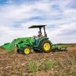 A person works in a farm field with a John Deere Compact Utility Tractor