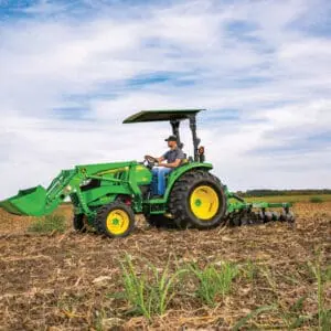 A person works in a farm field with a John Deere Compact Utility Tractor