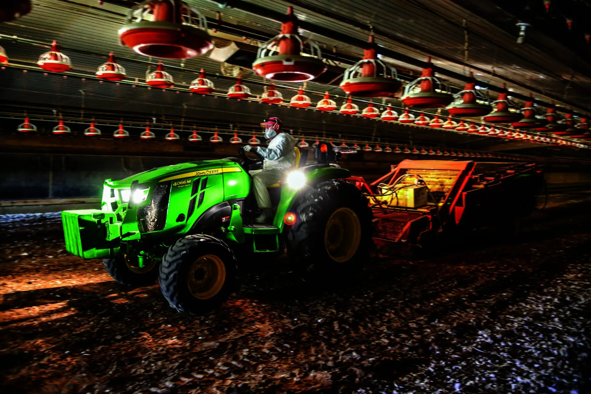 A poultry farmer works in a barn with a 4066M tractor