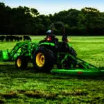 A person bush hogs a pasture with a John Deere 5066M