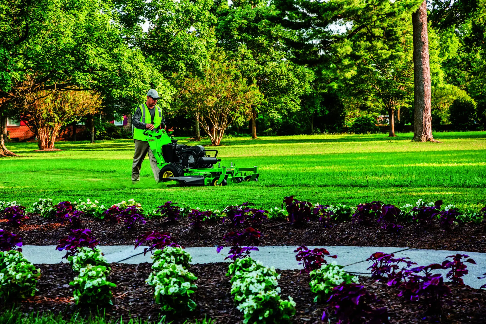 A person mows with a John Deere walk behind mower.
