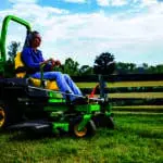 A woman mows along a fence with a Deere Z735M zero turn mower