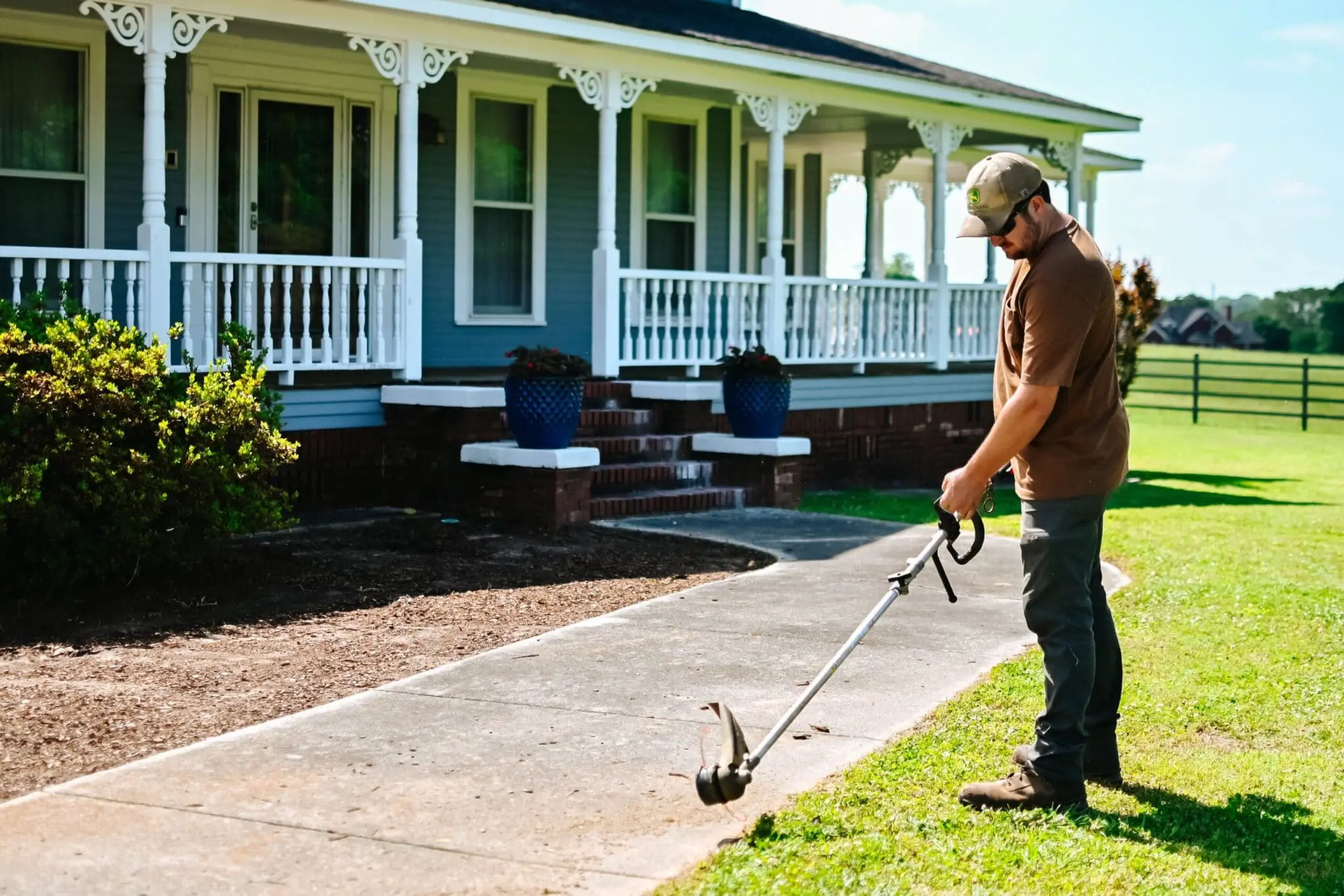 A person uses a trimmer to edge their sidewalk