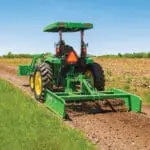 A person uses John Deere tractor and a land plane on a dirt road