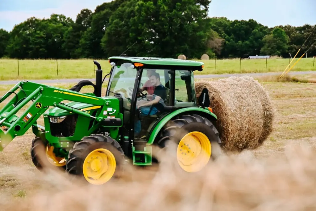 A person moves hay bales with a John Deere 5E tractor