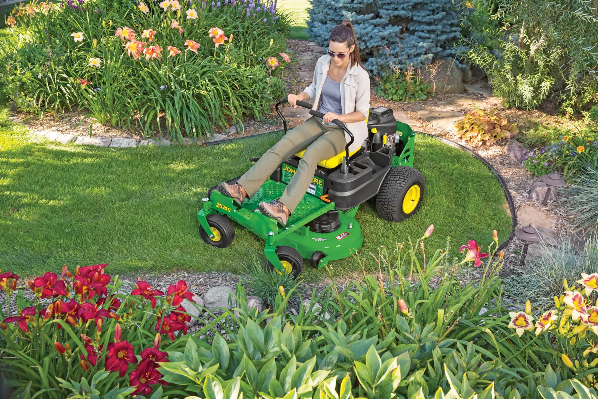 A person mows along flower beds with a Deere Z300 mower