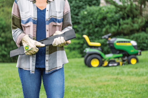 A person holds new John Deere mower blades in front of their mower
