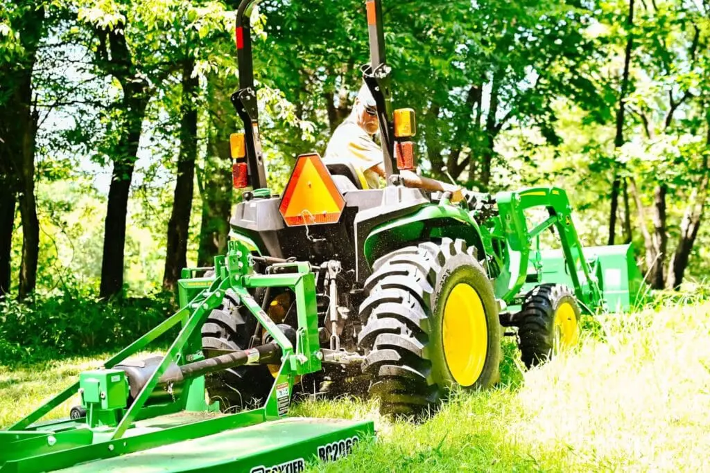 Man runs John Deere compact tractor with bush hog