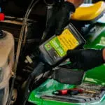 John Deere 4-cycle engine oil being poured into oil reservoir on John Deere riding lawn mower.