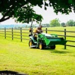 A man mows along a fenceline with a John Deere lawn tractor