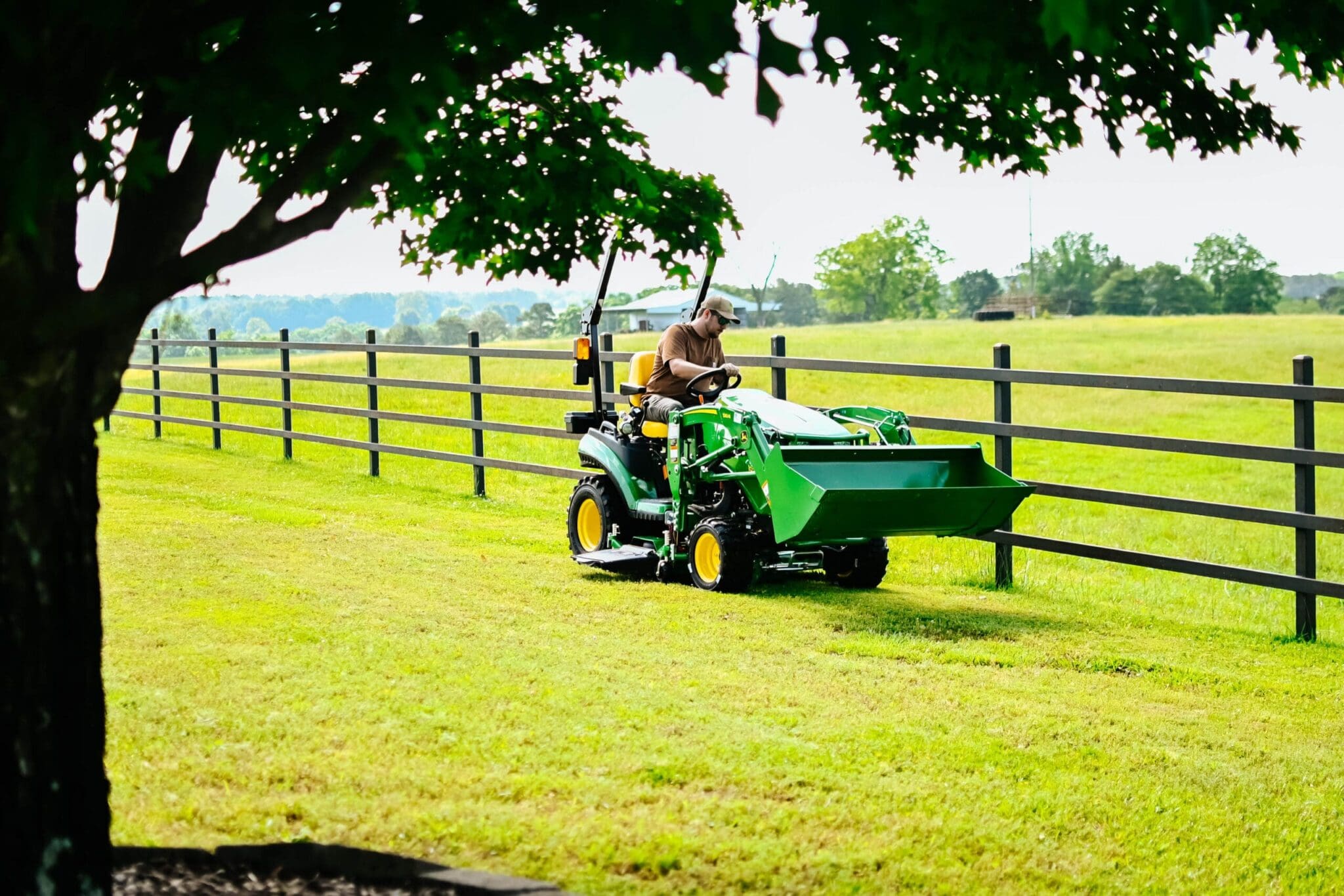 A man mows along a fenceline with a John Deere lawn tractor