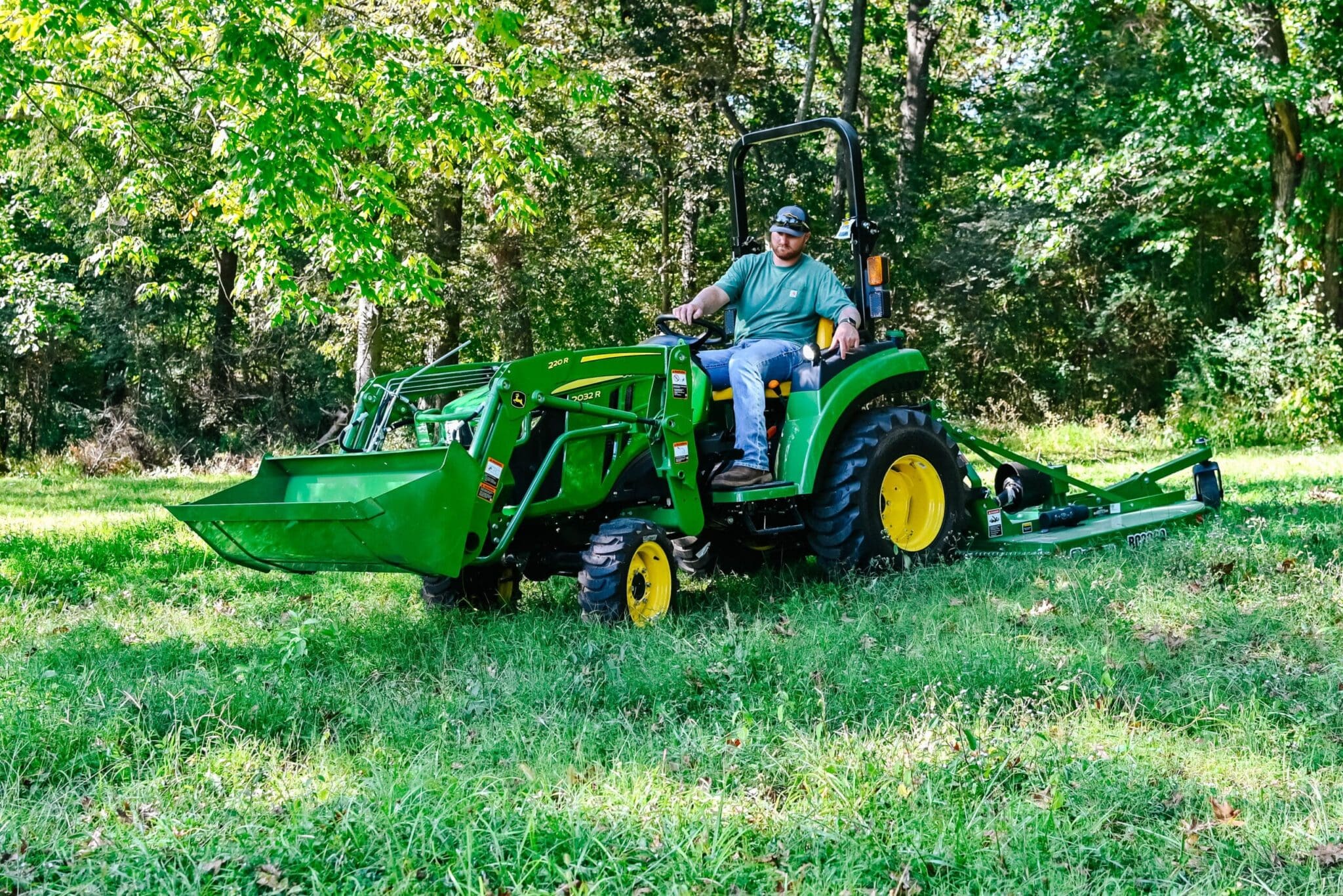 A person mows tall grass with a John Deere tractor and brush hog