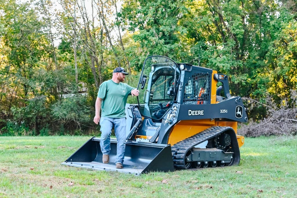 A person closes the door on a John Deere tracked skid steer