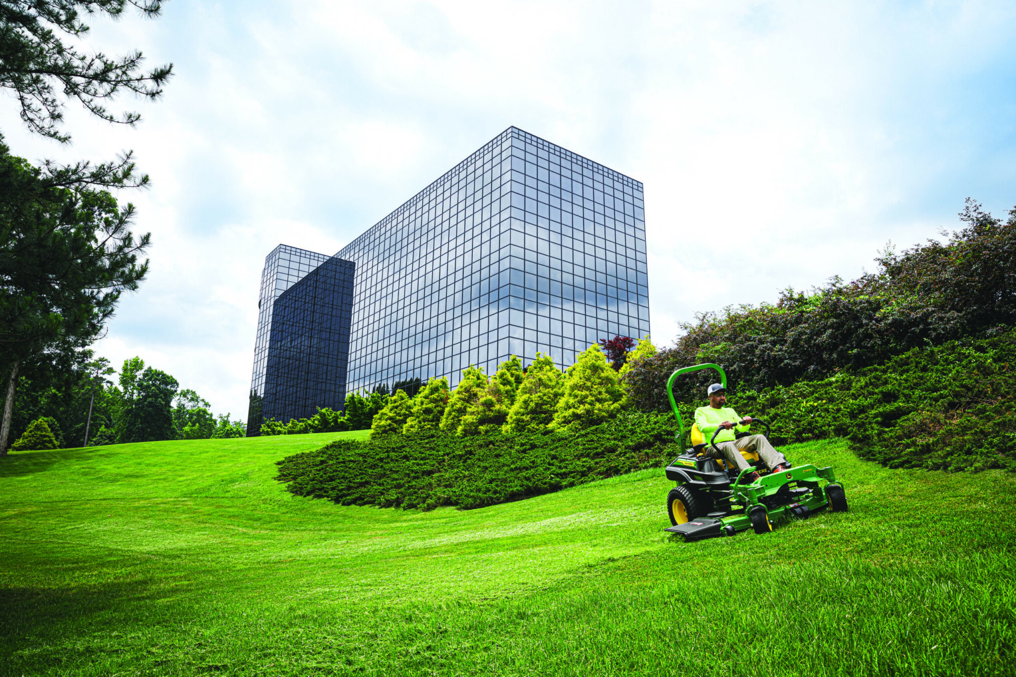 A landscape company mows along a hillside outside of an office building on a John Deere Z900 zero turn mower