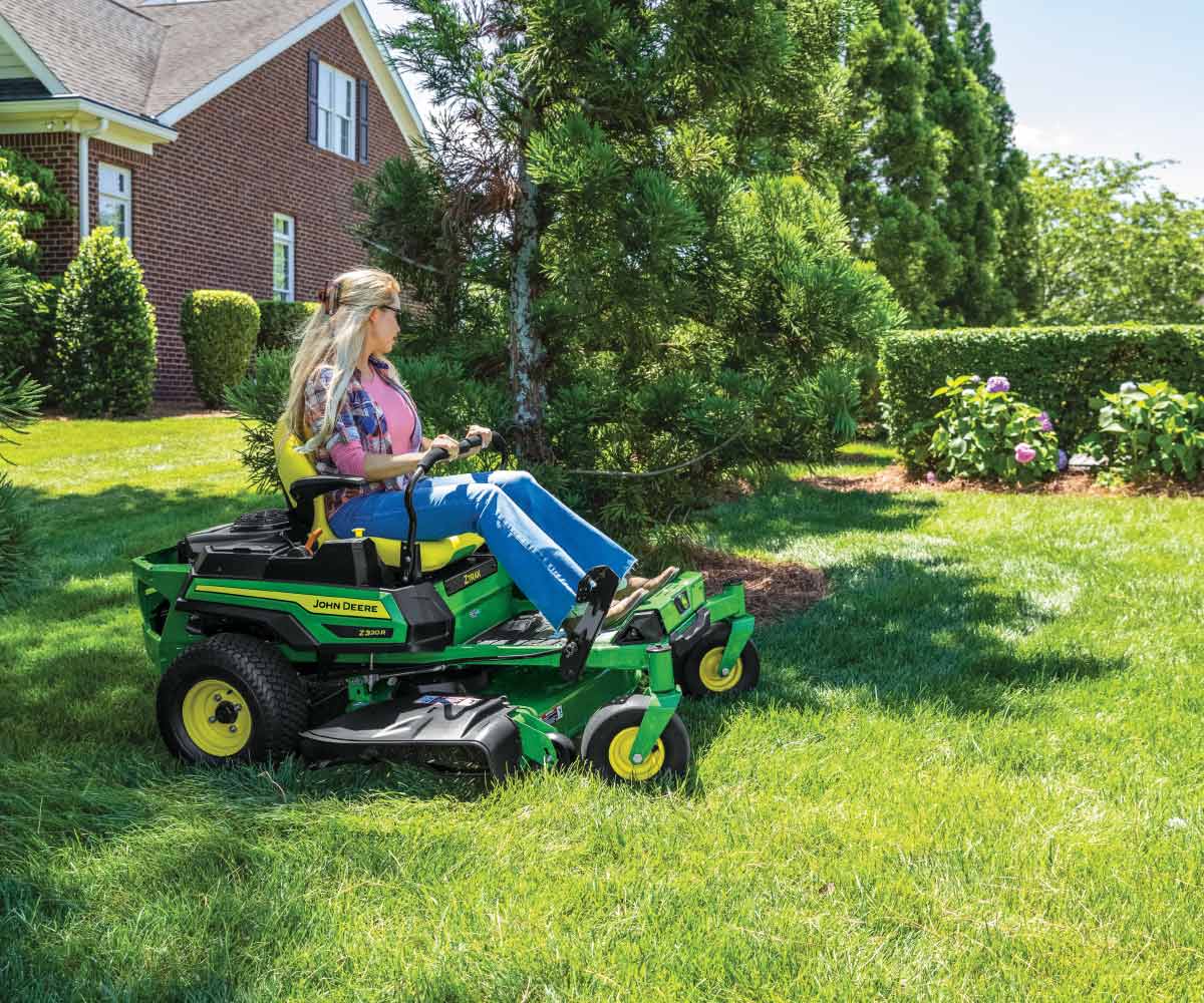 A woman mows a yard with a Z320M Deere zero turn