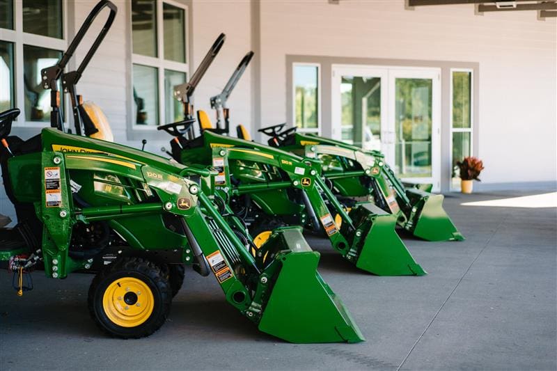 Three John Deere Compact tractors with loaders sit in front of TriGreen Equipment in Columbia.