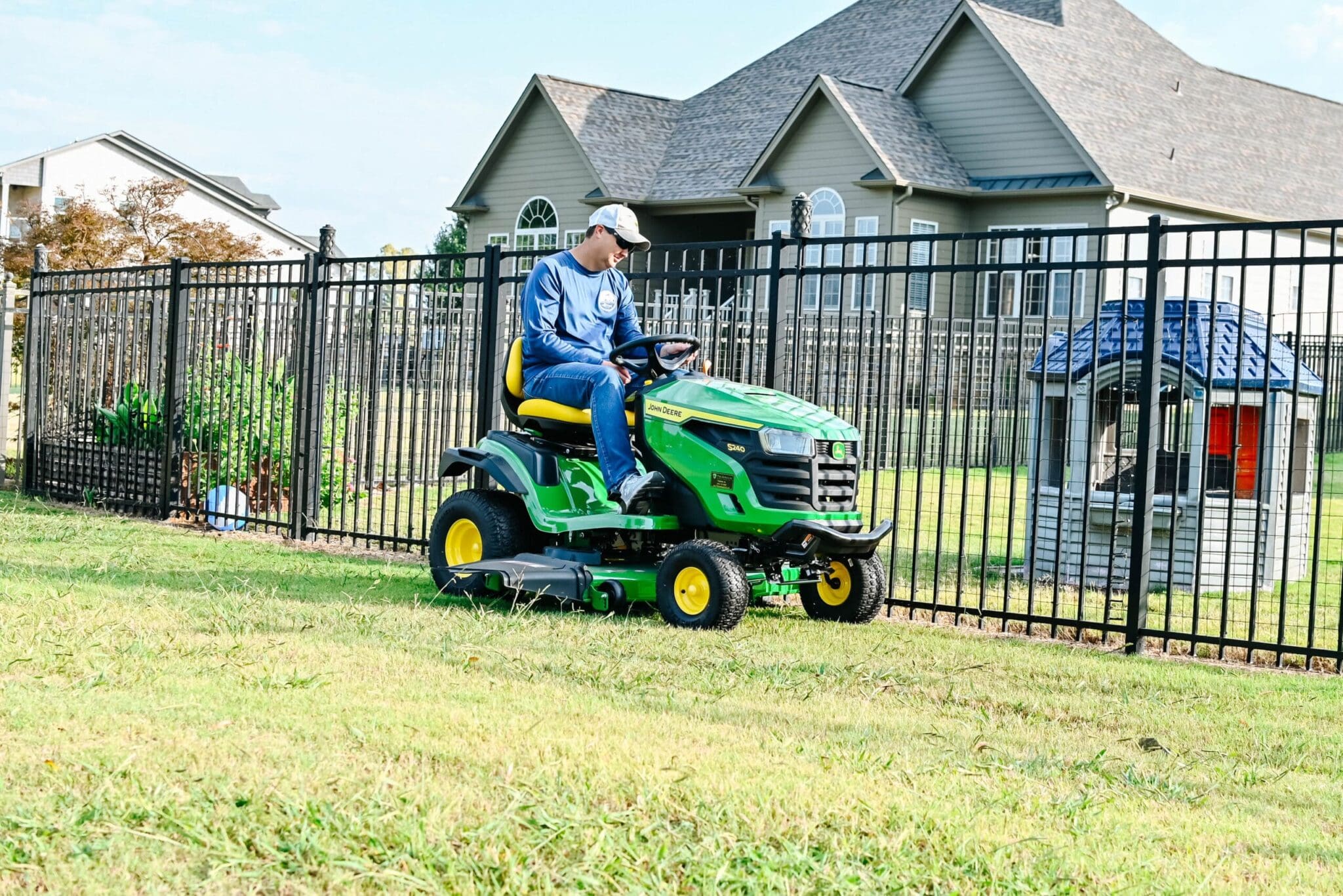 A man drives a John Deere S140 riding lawn mower in a backyard in Alabama